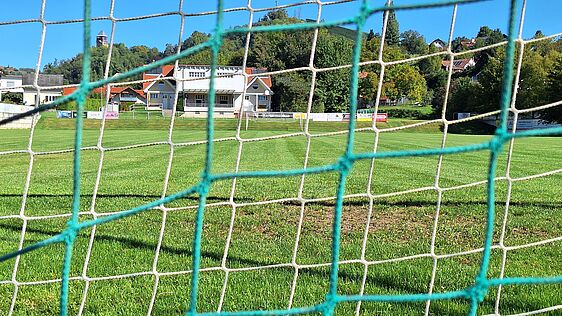 Betrachtung eines Sportrasenspielfeldes durch die Maschen des Ballfangzaunes